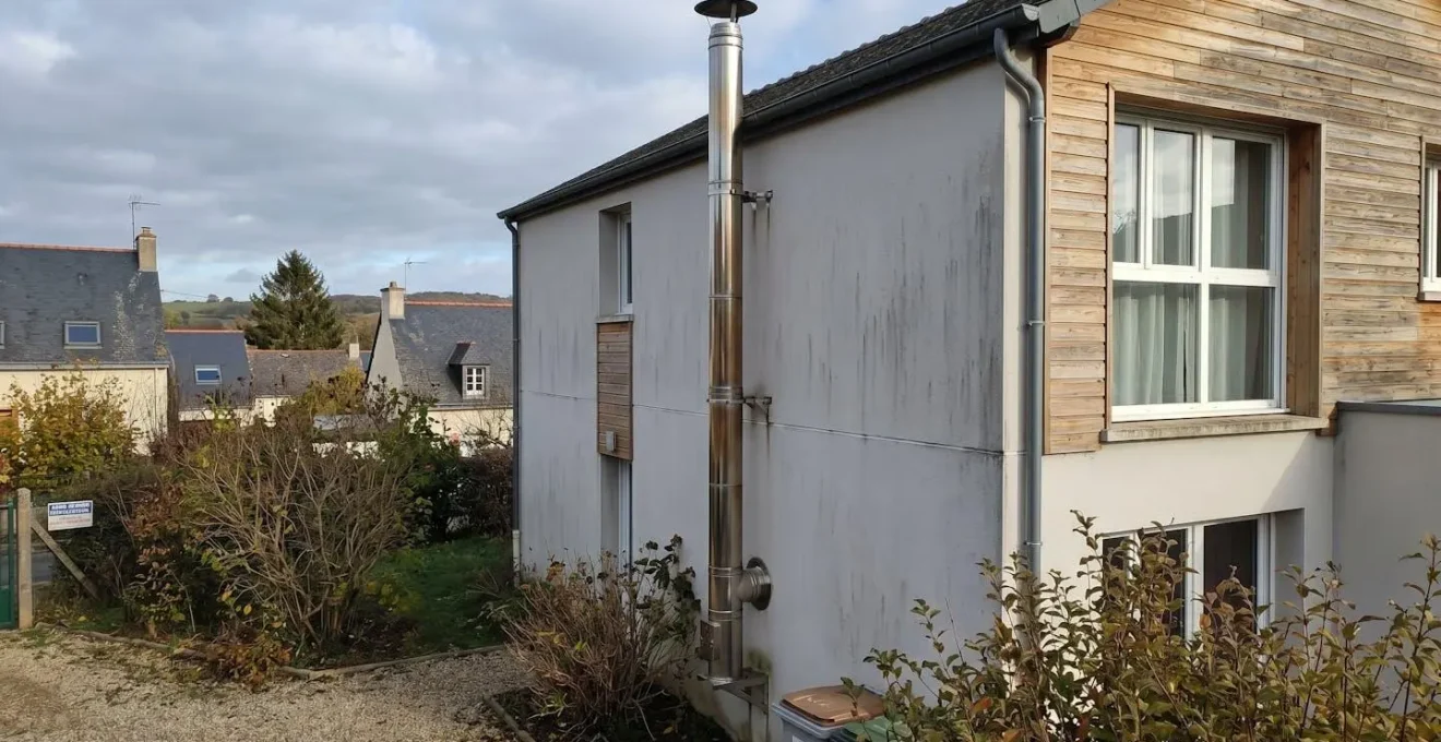 Conduit de fumée en inox double paroi fixé sur la façade d'une maison individuelle, avec chapeau anti-pluie visible en partie haute